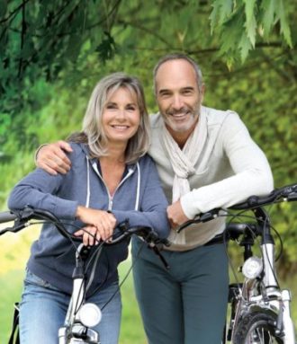 a happy mature couple pose while out for a bike ride in the park