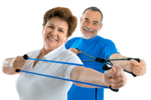 A mature couple smiling while exercising their upper body with resistance bands