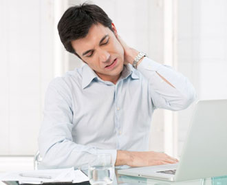 a young business man sitting at his desk is rubbing his sore neck.