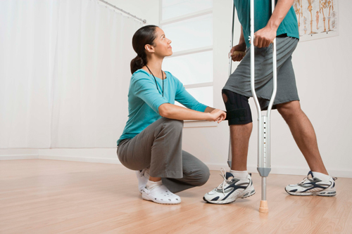 Physiotherpist and knee recovery this is an image of a young black physiotherapist working a male client with crutches and a knee brace